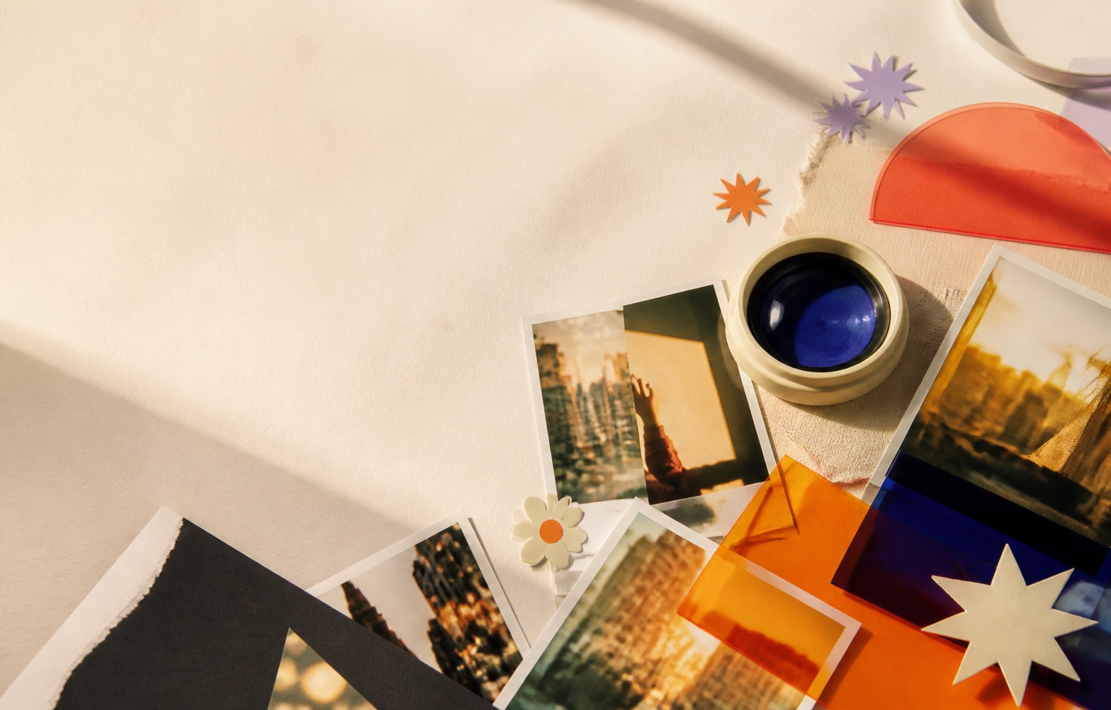 Printed photographs, colorful acetate and a camera lens arranged on a sunlit creative table